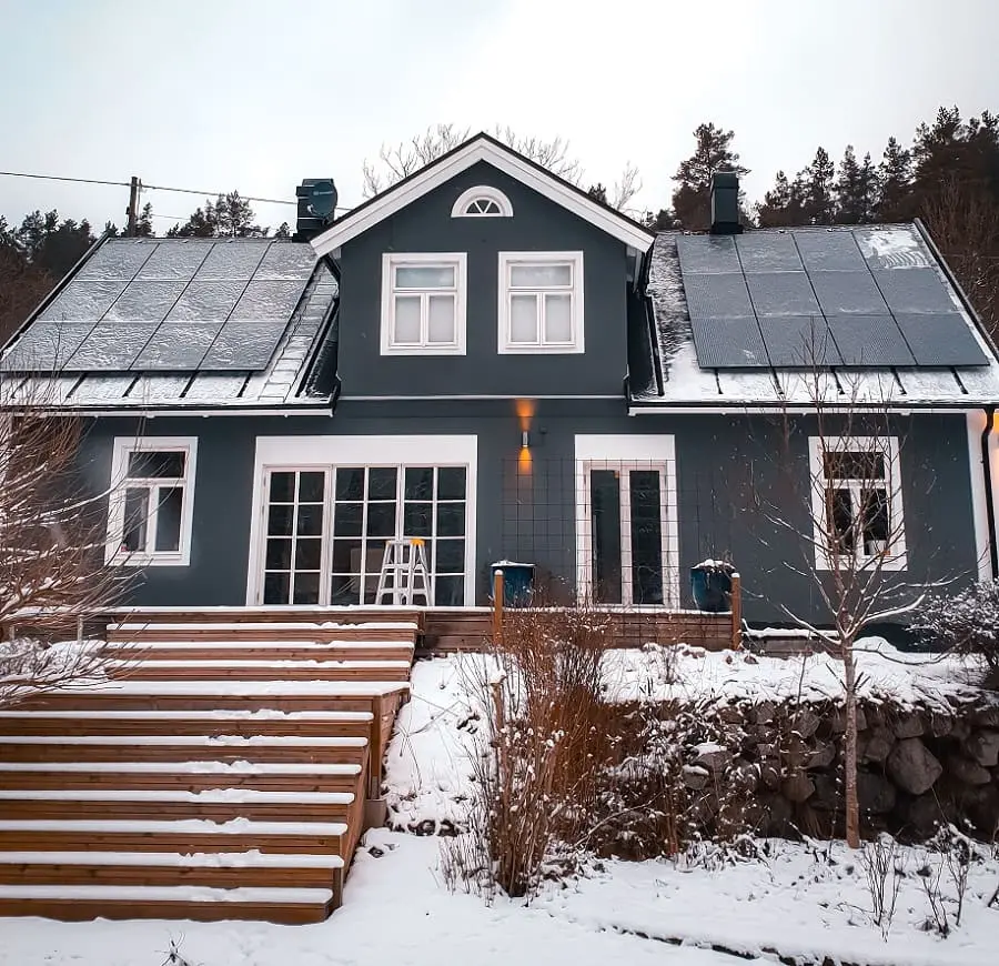 trädgård med snö och en villa med solceller
